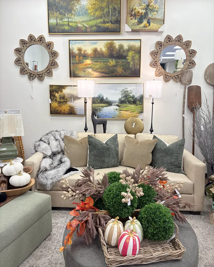 A sofa under a wall of landscape paintings, with an autumn centerpiece on the ottoman